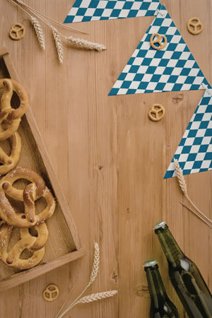Traditional Oktoberfest flat lay features Bavarian pretzels, golden wheat, green beer bottles, and blue and white checkered flags on a rustic wooden background, evoking German culture.の写真素材