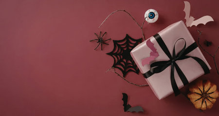 Beautifully wrapped pink gift box with black ribbon and pink butterflies surrounded by halloween decorations including spider web bats and eyeball on a pink background.の写真素材