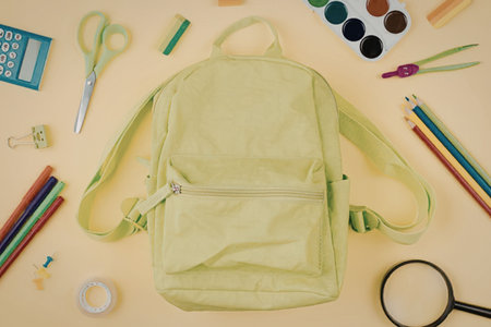 Bright green backpack surrounded by vibrant school supplies including colored pencils, scissors,...