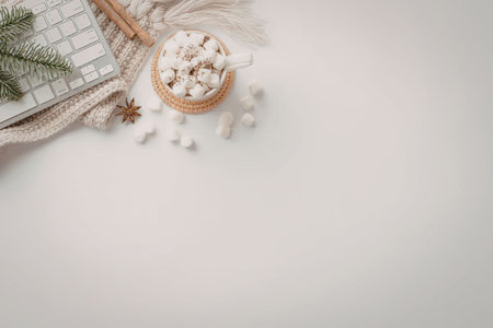 Hot chocolate with marshmallows and cinnamon sticks near a keyboard and evergreen branches on a white textured sweater on a white background.の写真素材
