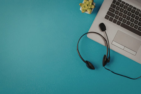 Modern laptop and black headset on a blue background with a small potted plant nearby creating a...