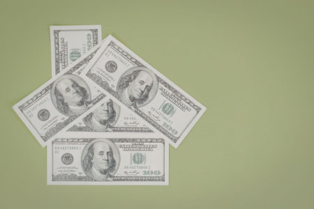 Four one hundred dollar bills are arranged in a loose pile on a vibrant green background symbolizing...