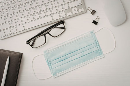 Face mask placed on a white office desk surrounded by computer accessories and stationery items...