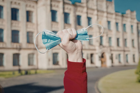 Person raises fist in triumph holding discarded face masks outside a historic building on a sunny...