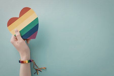 Hand holding a rainbow colored heart symbolizing love and support for the lgbtq community during pride month with a matching rainbow wristband on a blue background.の写真素材