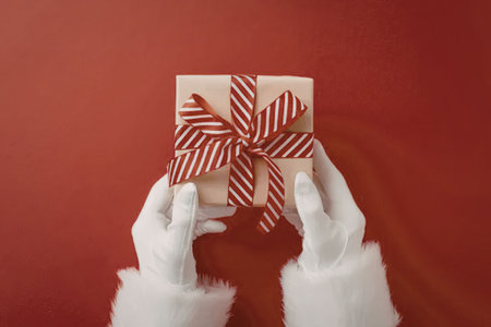 Santa claus hands in white gloves holding a beautifully wrapped christmas gift box with a red and...
