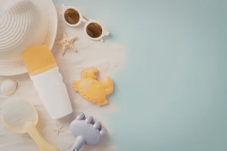 Summer essentials like sunscreen lotion, beach toys, and accessories are arranged on a sandy surface...