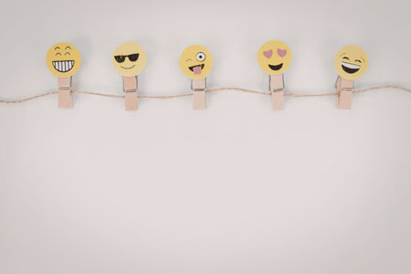 Five different yellow emojis with various facial expressions attached to a clothesline using wooden...