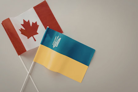 Handheld Canadian and Ukrainian flags are crossed against a simple light background symbolizing bilateral relations and international partnership between the two proud nations.の写真素材