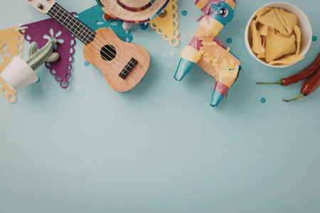 Colorful mexican party decorations and accessories including ukulele sombrero pinata cactus and bowl of tortilla chips with chili peppers on a blue background.の写真素材