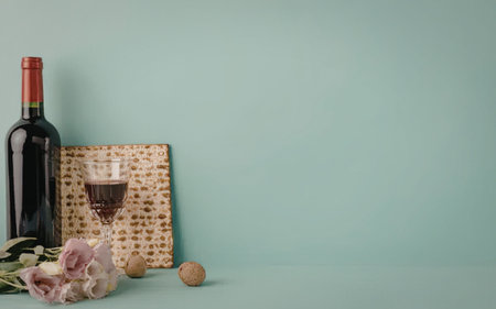 Wine bottle and glass accompanied by flowers and matzo on a pastel blue background symbolizing...