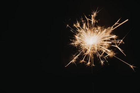 A bright sparkler firework glowing with sparks against a black background