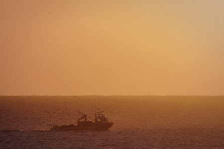 A boat sailing on the ocean during sunset with a vibrant orange sky in the background.