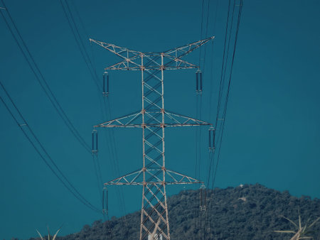 A tall metal power line tower with electrical wires stretching across a clear blue sky.