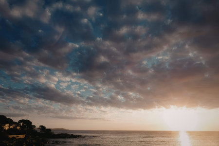 A peaceful sunset scene with a cloudy sky, shining sun, and calm ocean waters