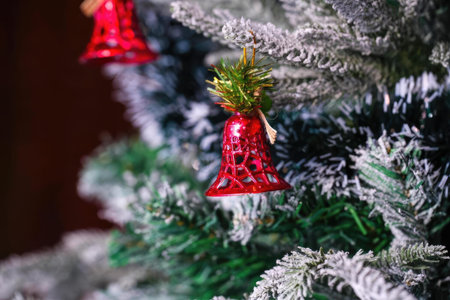Close-up of a decorated Christmas tree with red bell ornament and green pine branches, festive and cozy holiday decor.