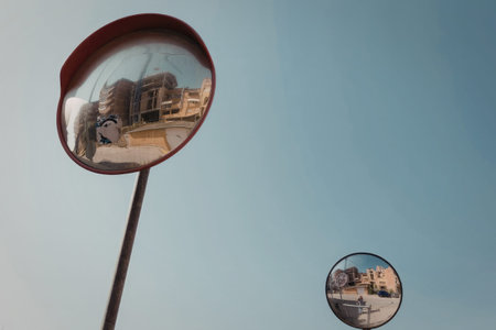 Two convex street mirrors reflecting buildings, sky, and street scene