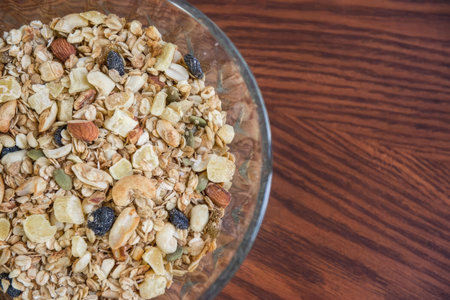 A detailed view of assorted nuts in a glass bowl on a wooden surface, healthy snack