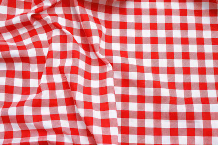 Close-up of a red and white checkered tablecloth with folds and shadows outdoors.