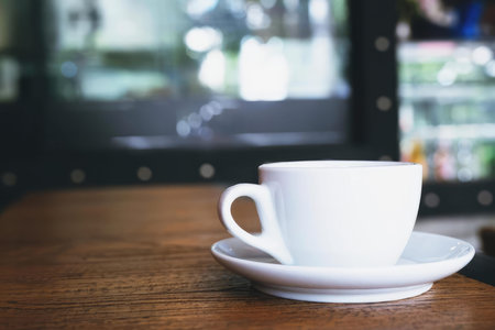 A simple photo of a white coffee cup on a saucer placed on a desk with a computer screen in the background.