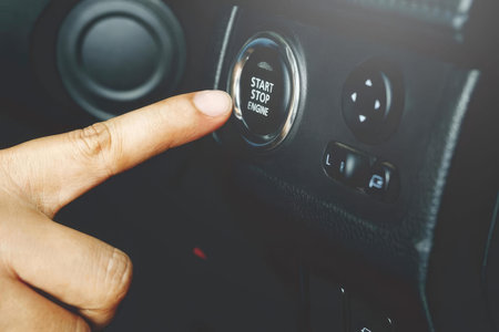 A personâ€™s finger pressing the start stop engine button in a car interior