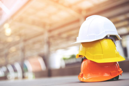 A stack of yellow, orange, and white helmets in a sunny construction setting.