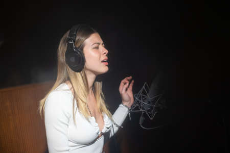 Portrait of excited female singer recording song in studio. Young Caucasian woman singing at radio or sound recording studio. Creating music conceptの写真素材