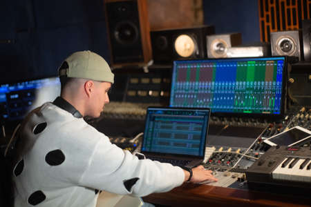 Young music producer working in sound recording studio. Sound engineer sitting at laptop and mixing console panel. Creating music conceptの写真素材