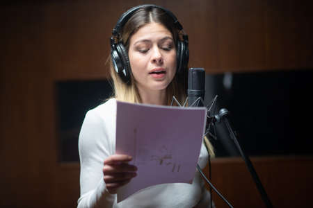 Portrait of young female performer recording song in studio. Caucasian woman holding text and singing song on radio or at sound recording studio. Creating music conceptの写真素材