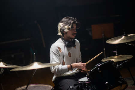 Concentrated young man training on drum set in studio. Musician with headphones rehearsing or recording drums. Drummer training conceptの写真素材