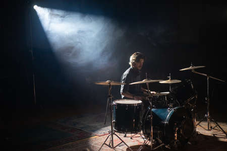 Young drummer sitting in spotlight and training in hall. Concentrated rock musician rehearsing or recording drums. Drummer training conceptの写真素材