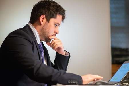 Side view of attentive man working. Man in suit sitting at table and using laptop with charts on screen. Business, job, occupation, late night work conceptの写真素材