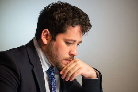Portrait of young businessman thinking. Man with curly hair in suit looking down. Business, job, occupation, late night work conceptの写真素材