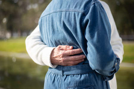 Close-up of aged mans hand hugging woman in park. Careful man and woman resting in public park and man gently hugging womans waist and holding hands. Relations, romance and love of aged people conceptの写真素材