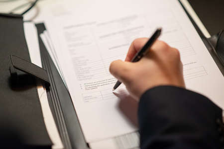 Close-up of businessperson writing. Male hand writing with pen on white sheet of paper, signing contract. Business, job, occupation, late night work conceptの写真素材