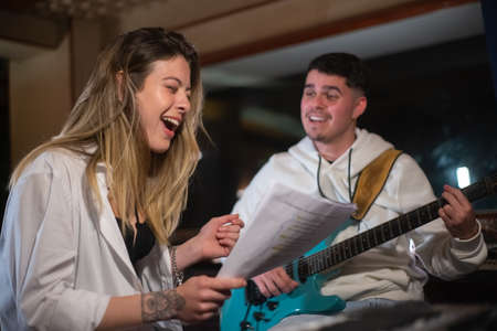 Music band rehearsing song in sound recording studio. Excited young Caucasian woman singing and man playing electric guitar. Creating music conceptの写真素材