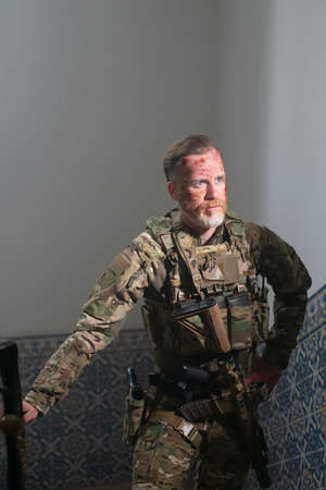 Weary army man resting after battle. Caucasian man with beard with smears of blood on face standing upstairs. Military, army, danger, fighting, airsoft conceptの写真素材