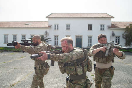 Portrait of courageous soldiers during battle. Men with blood smears on faces near house, aiming. Military, army, teamwork, fighting, airsoft conceptの写真素材