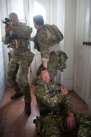 Armed men helping wounded friend. Caucasian men with carrying injured teammate. Military, army, danger, fighting, airsoft conceptの写真素材