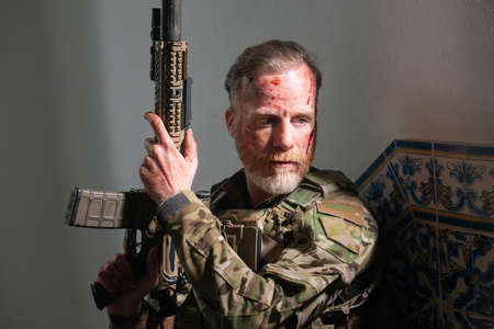 Attentive army man during battle. Caucasian man with beard with smears of blood on face holding...
