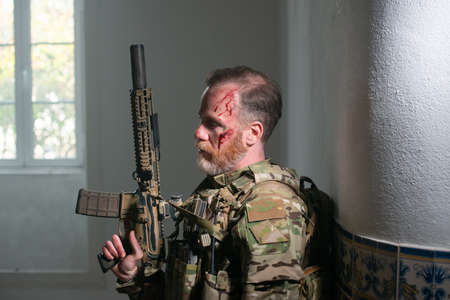 Watchful military man during battle. Caucasian man with beard with smears of blood on face holding machinegun. Military, army, danger, fighting, airsoft conceptの写真素材