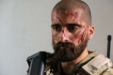 Portrait of sad man in military uniform. Caucasian man with beard with smears of blood on face....