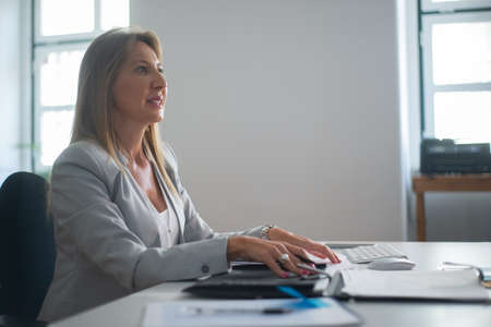 Portrait of businesswoman at work desk. Thoughtful woman in formalwear sitting at table with pen and...