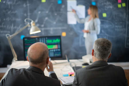Back view of company experts working in office. Two serious man in formalwear sitting looking at...
