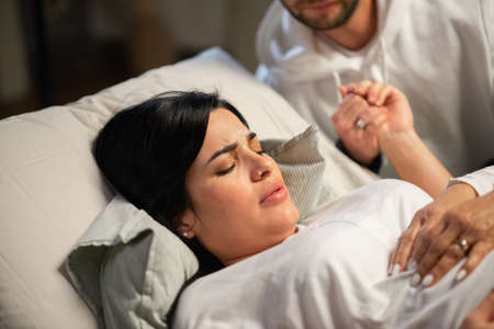 Concentrated woman giving birth at home. Woman with pierced nose lying, feeling contractions during...