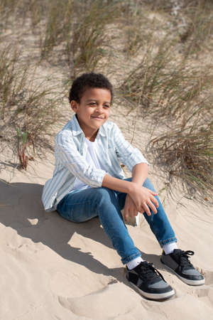 Portrait of beautiful African American boy. Male model with curly hair in casual clothes sitting on...