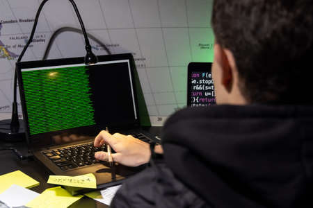 Back view of man planning hacker attack. Man in coat using laptop, typing code. Hacking, technology,...