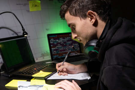 Side view of man planning hacker attack. Man with headphones sitting at laptop with code, writing in...