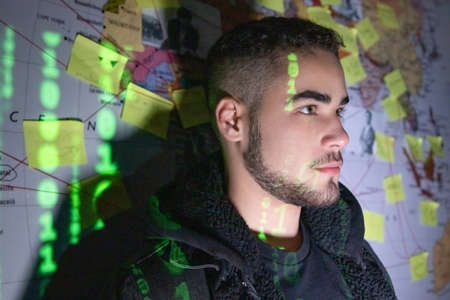 Portrait of good-looking man in dark room. Man with beard standing near wall with stickers,...