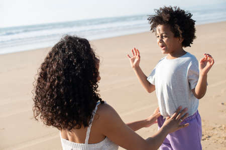 Happy mother and daughter spending time on beach. African American family walking, laughing,...